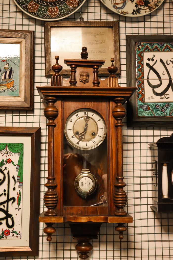 Antique wooden clock surrounded by artistic wall decor and calligraphy.