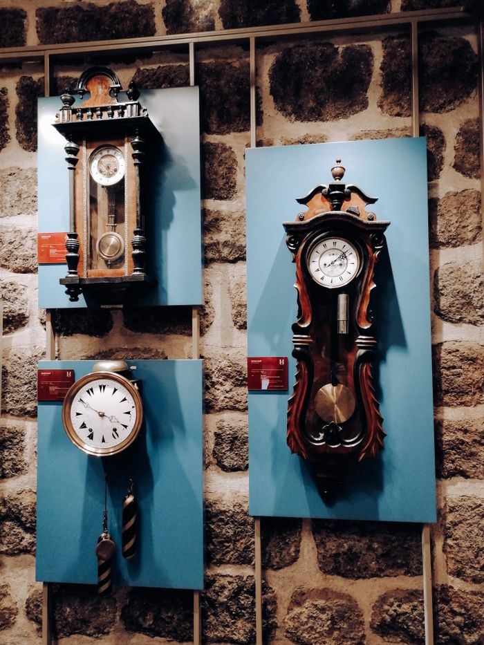 Three vintage wall clocks on display against a rustic stone background.